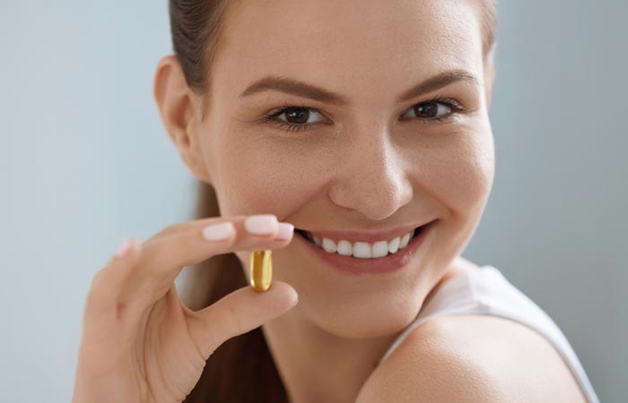Femeie zâmbitoare ținând capsulă de vitamina E
